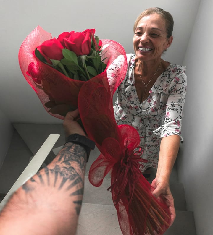 A mom with a big smile on her face is receiving a bouquet of flowers from her son.